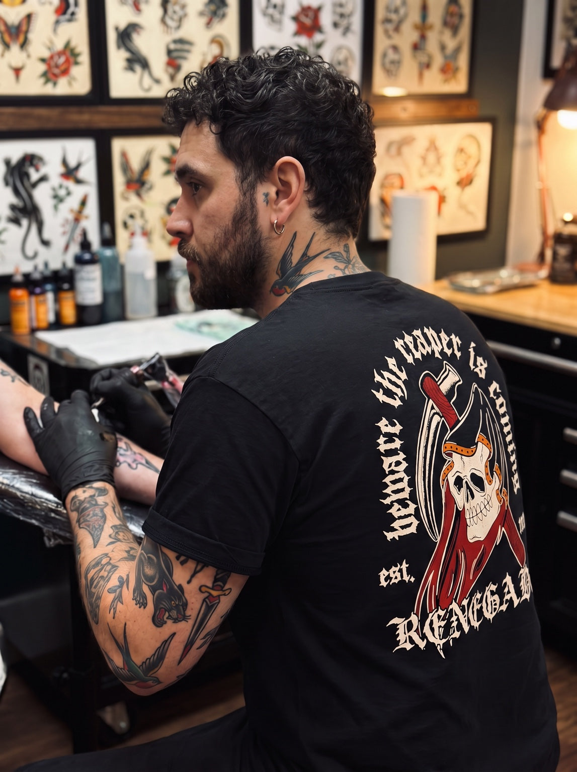 Tattoo artist wearing an Original Renegade reaper graphic T-shirt in a tattoo studio