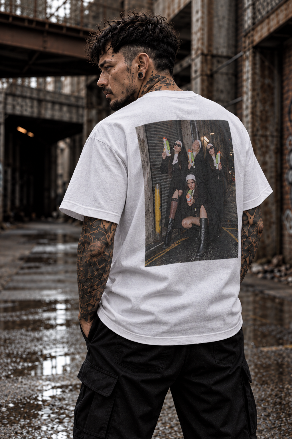 Super Sinner white graphic tee on tattooed male model in industrial setting, rear three-quarter view